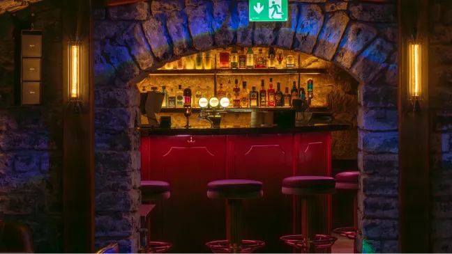 A red alcove with bar stools and illuminated bottle shelves.