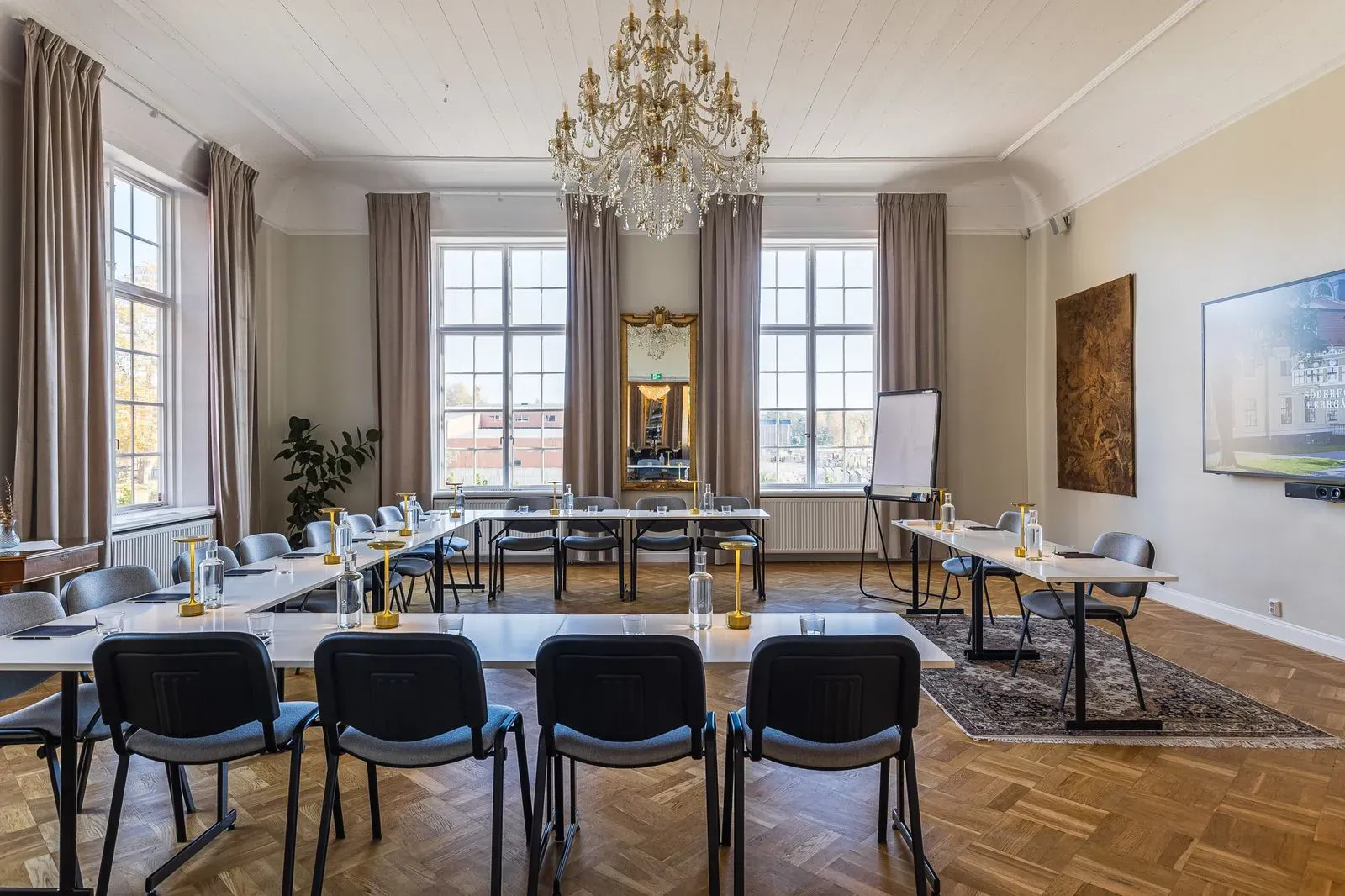 Bright conference room with U-shaped tables, tall windows, and a chandelier.
