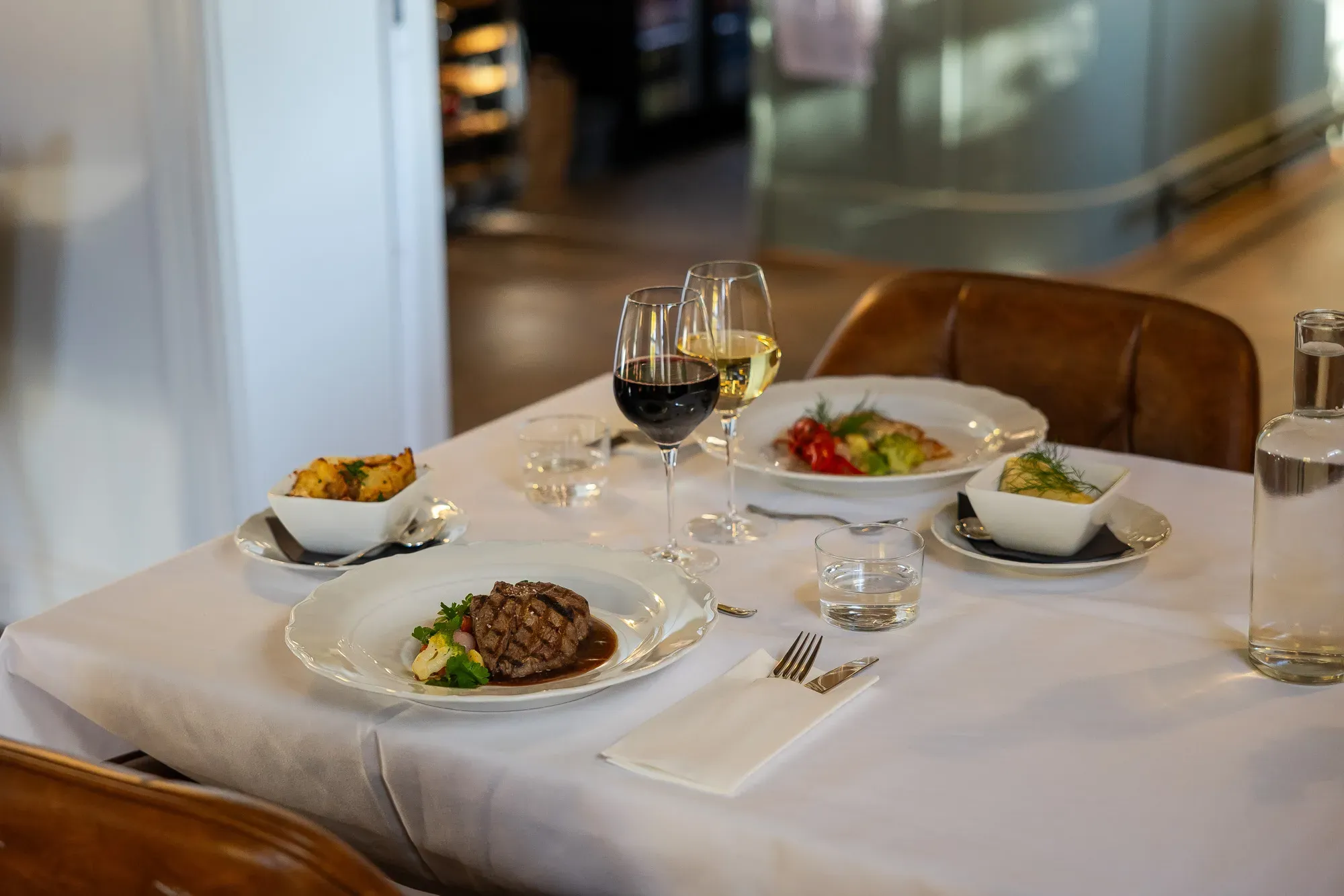 Gedeckter Esstisch mit mehreren Gerichten und Wein im Herrenhausrestaurant.