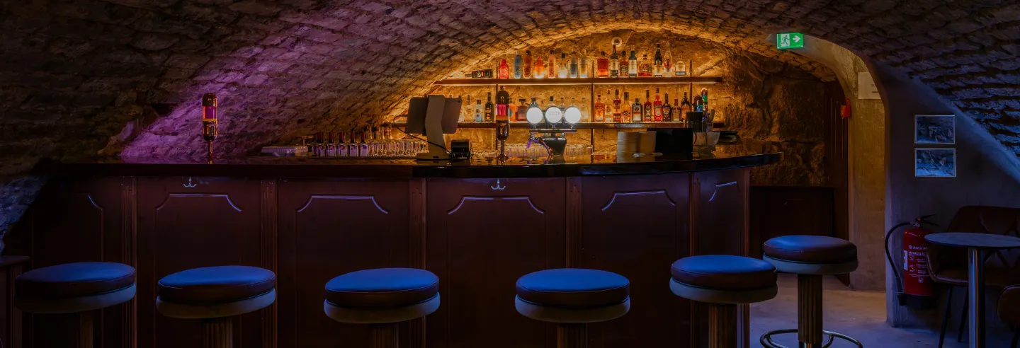 The bar inside the vaulted cellar, with illuminated bottle shelves.