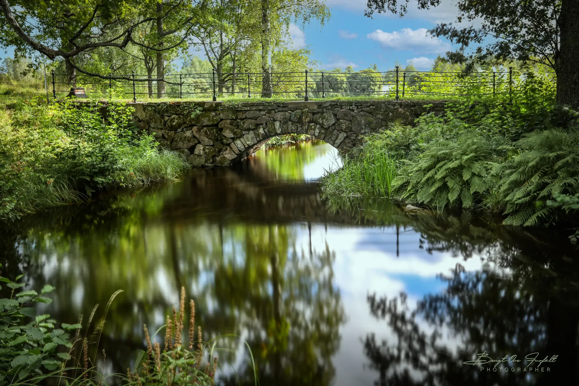 Stone bridge over a still stream in the green English park.