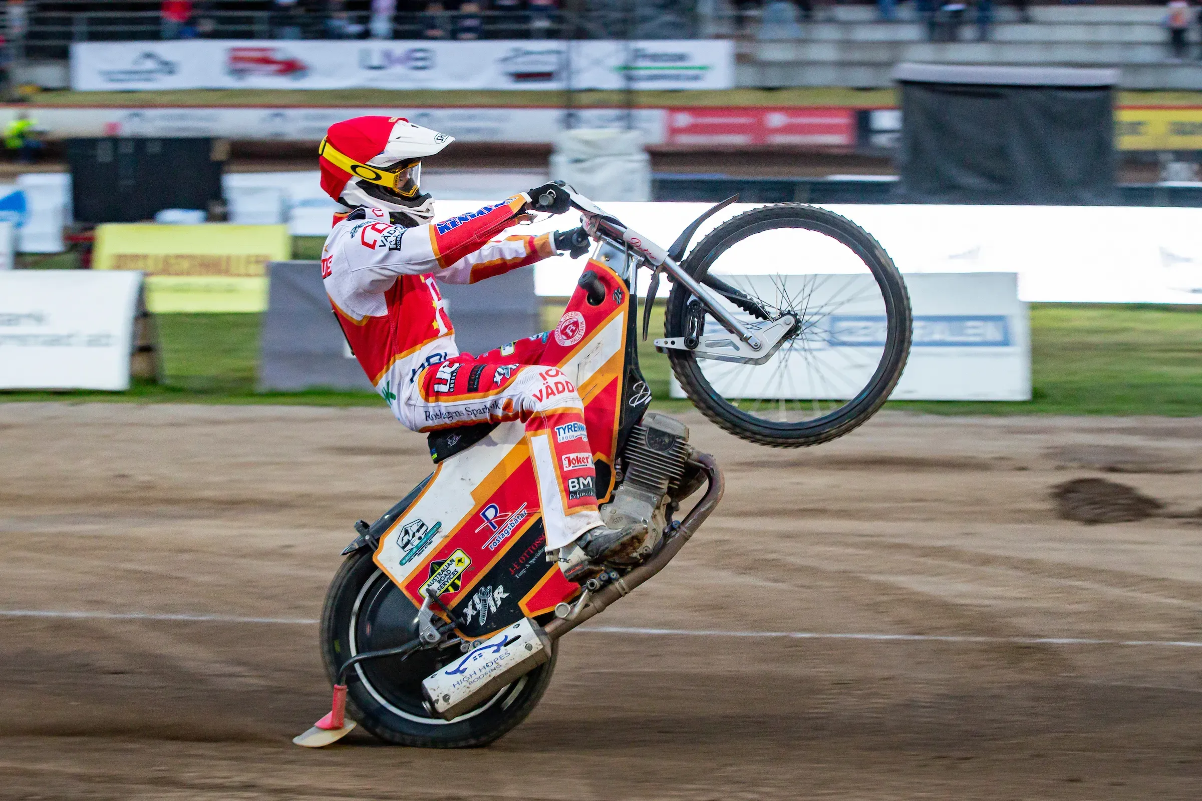 Speedway rider performing a wheelie during a race.