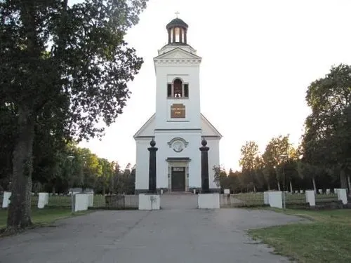 Helle Fassade und Turm der Kirche von Söderfors im Grünen.