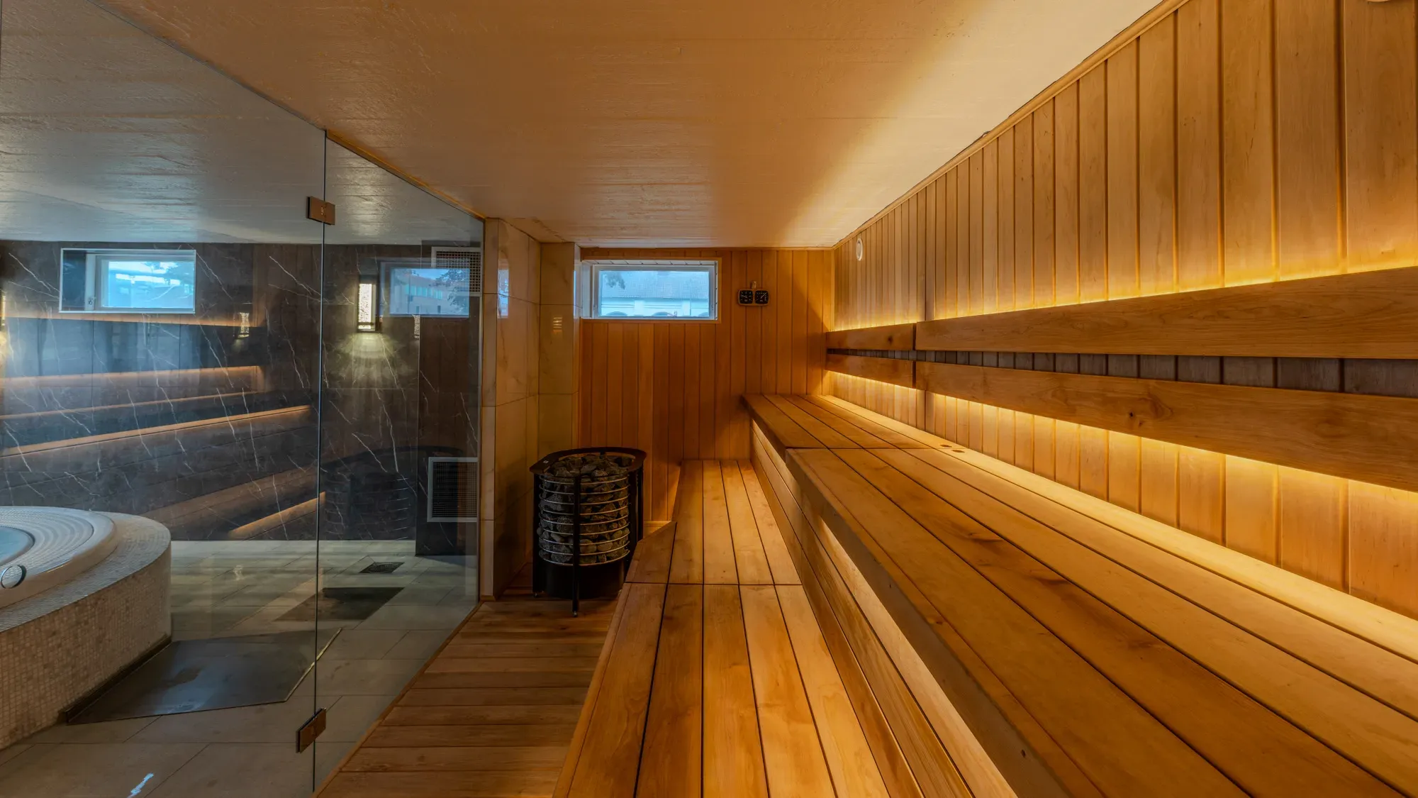 Warm beleuchtete Sauna mit Holzbänken und Glaswand.