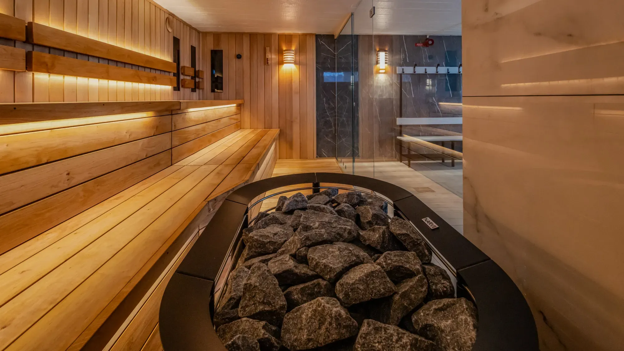 Warm beleuchtete Sauna mit Holzbänken und Saunaofen.